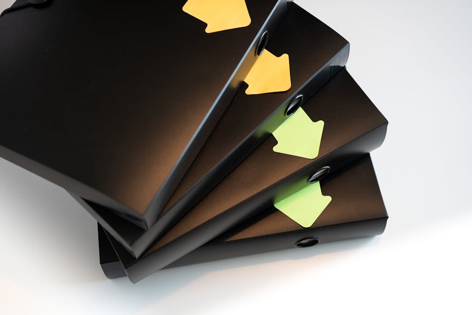 A stack of black ring binders with yellow and green labels for organization.